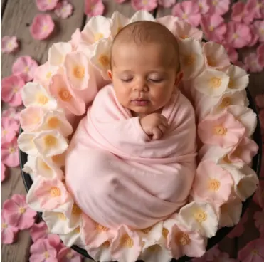 Newborn swaddled in a floral wrap, resting on a petal nest, AI-generated